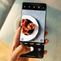 Ręka trzyma telefon, na ekranie którego widać trzy ptysie polane czekoladą. Robione są zdjęcia z telefonu.