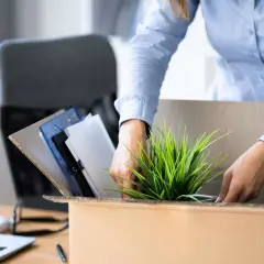 Frau packt ihre Bürosachen in einen Karton, um einen ausstand zu geben. Ein Laptop und Ordner sind zu sehen.