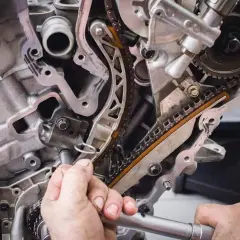 Mechanik pracuje przy rozrządzie silnika. Zbliżenie na łańcuch rozrządu i napinacz. Objawy zużytej poduszki silnika mogą być różne.