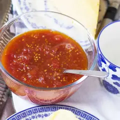 En skål med tomatmarmelad, perfekt för ett enkelt tomatmarmelad recept. Serveras med en sked och en blåvit kopp.