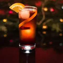 Elegancki drink z campari, lodem i pomarańczą, na tle świątecznych światełek.