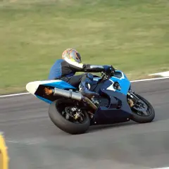 Piloto de MotoGP en plena curva, con la moto azul inclinada y llamas saliendo del escape. ¡Un auténtico holeshot!