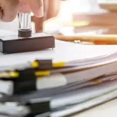 Dłoń z pieczątką nad stosem dokumentów, symbolizującym formalności związane z podatkiem od spadków i darowizn.