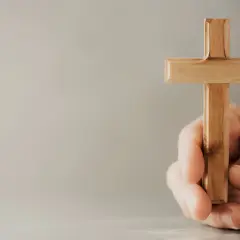Eine Hand hält ein hölzernes Kreuz, ein Symbol, das Christen weltweit verbindet.