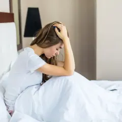 Mujer joven en la cama, con la cabeza entre las manos, sintiendo **ansiedad al despertar**.