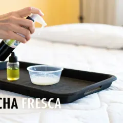 Mano rociando limpiador sobre una bandeja con líquidos, parte de un tutorial sobre como limpiar un colchon.