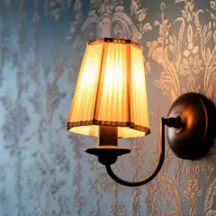 Aplique de pared rústico con pantalla plisada iluminada sobre papel tapiz floral.