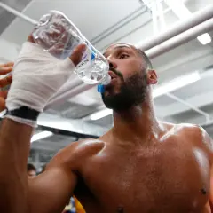 A boxer, hand-wrapped, drinks from a water bottle. This shows why boxers spit out water: to stay hydrated without swallowing too much.