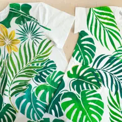 Deux t-shirts blancs ornés de motifs de feuilles tropicales peintes à la peinture acrylique sur tissu. Une touche de doré sur une fleur.