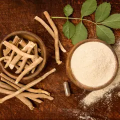 Ashwagandha roots, powder, and capsules on a wooden surface with leaves.
