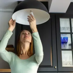 Mujer cambia bombilla en lámpara. ¿Se puede vender una casa sin luz ni agua? Quizás, pero con luz es más fácil.
