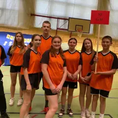 Uczniowie zespołu szkolno przedszkolnego SP GAC w pomarańczowych strojach sportowych pozują do zdjęcia w sali gimnastycznej.