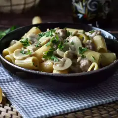 A bowl of rigatoni pasta with creamy mushroom and sausage sauce, garnished with parsley.
