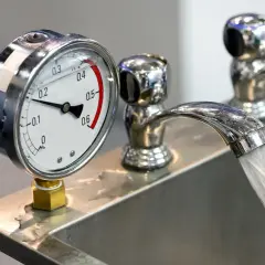 Manometro che misura la pressione dell'acqua in un lavandino. Il rubinetto eroga acqua, indicando la pressione alta acqua calda o fredda.