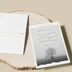Zwei Postkarten auf einem Holzstamm. Eine zeigt einen Baum im Nebel und den Spruch: "Der Herr ist denen nahe, die verzweifelt sind und rettet diejenigen, die alle Hoffnung verloren haben.