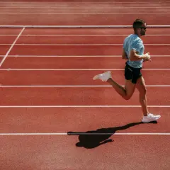 Mężczyzna w niebieskiej koszulce i czarnych spodenkach biegnie po bieżni lekkoatletycznej.