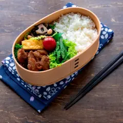 A bento box filled with rice, fried chicken, tamagoyaki, asparagus, and a cherry tomato. This is what comes in a bento box for a delicious meal.