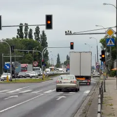 Kierowca srebrnego sedana decyduje się na przejazd na żółtym świetle, mimo że sygnalizator obok świeci na czerwono.