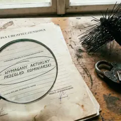 Ubezpieczenie lokalu wymaga aktualnego przeglądu kominiarskiego. Jak obliczyć wartość odtworzeniową lokalu? Stare dokumenty, lupa i szczotka kominiarska.