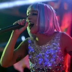 Lorena Castell, con peluca rosa y azul, canta en un escenario con un vestido brillante.