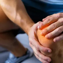 Ból kolana, który może być objawem dyskopatii lędźwiowej, dotyka mężczyznę trzymającego się za bolącą kończynę.
