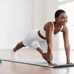 Frau in weißer Sportkleidung macht Liegestütze auf einer Matte. Sie lächelt und genießt ihr Kraft Training.
