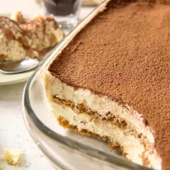 Najprostsze tiramisu w szklanej formie, posypane kakao. Na talerzyku porcja deseru i łyżeczka.