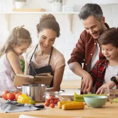 Famille préparant un repas. Le père aide son fils à couper des légumes. La mère et la fille consultent un livre de recettes. On se demande : lactose c'est quoi ?