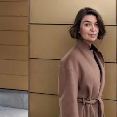Cecilia Hansson, klädd i en brun kappa, står framför en modern guldfärgad vägg.