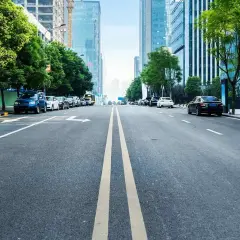 Eine Straße mit einer **durchgezogenen Linie** in der Mitte, gesäumt von Bäumen und modernen Gebäuden. Autos parken am Straßenrand.