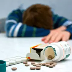 Osoba w bluzie leży na stole, obok rozsypane tabletki, w tym **setaloft**.