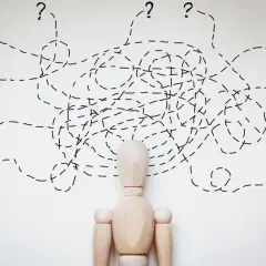 Drewniany manekin z chaotycznymi liniami i znakami zapytania nad głową, symbolizującymi trudności w diagnozie, np. borderline ICD 10.