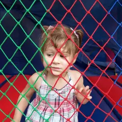 Mała dziewczynka w kratkowanej sukience patrzy przez kolorową siatkę. Może słucha piosenki dla małych dzieci.