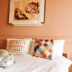 Chambre couleur terracotta avec un lit douillet, des coussins colorés et une peluche chat. Un tableau de lapins orne le mur.
