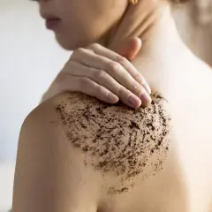 Una mano aplica exfoliante corporal de café en el hombro. Aprende como usar exfoliante corporal para una piel suave.