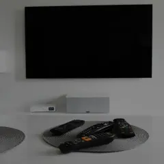 Na stole leżą piloty, a czarny ekran telewizora sugeruje, że jest brak obrazu.