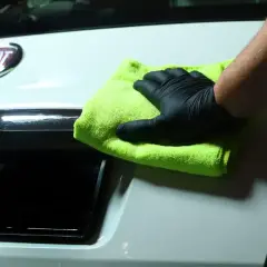 Ręka w czarnej rękawiczce poleruje białą klapę bagażnika Fiata zieloną mikrofibrą. Po pracy można sięgnąć po zimne alkohol IPA.