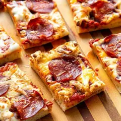 Kawałki pizzy pepperoni na desce. Dowiedz się, jak podgrzać pizzę na patelni, by była idealnie chrupiąca.