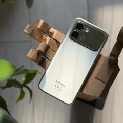 Srebrny smartfon Infinix, marka znana z innowacyjnych rozwiązań, prezentuje się na drewnianej dłoni.