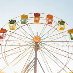 Grande roue colorée avec des nacelles jaunes, vertes, oranges et rouges sous un ciel clair.