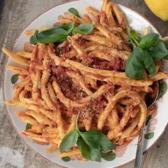 En skål med nduja pasta, toppad med färsk basilika och en citron i bakgrunden.