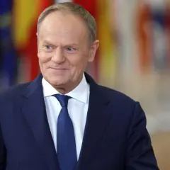 Uśmiechnięty Donald Tusk w granatowym garniturze i białej koszuli z niebieskim krawatem. Dziś Tusk robi wrażenie zadowolonego.
