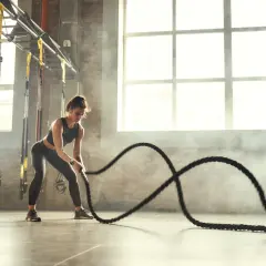 Kobieta wykonuje trening crossfit z linami bojowymi w siłowni.