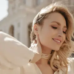 Uśmiechnięta blondynka z perłową opaską i naszyjnikiem. Różne rozmiary łańcuszków podkreślają jej szyję.