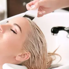 Kobieta z blond włosami w salonie fryzjerskim, gdzie nakładany jest jej kolor.