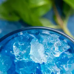 Intensywnie niebieski likier Blue Curacao z kruszonym lodem w szklance, z zielonym liściem w tle.