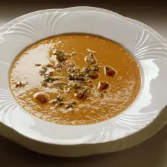 Aksamitny krem z pieczonej papryki, udekorowany świeżym tymiankiem i chrupiącymi grzankami, podany w eleganckiej białej misce.