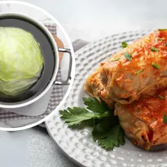 Jak sparzyć kapustę na gołąbki? W garnku gotuje się całą główkę, by liście łatwo odchodziły. Obok gotowe, pyszne gołąbki w sosie.