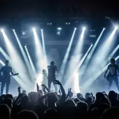 Zespół gra na scenie, oświetlony snopami światła. Tłum szaleje na koncercie w Krakowie.