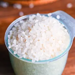 A measuring cup filled with short-grain white rice, ready for cooking Japanese rice.